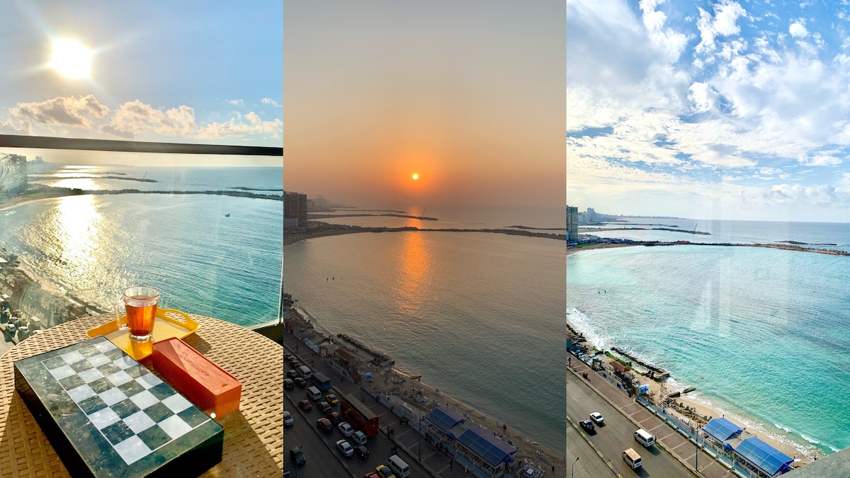A spacious terrace offers a view of the sea and horizon, with sunlight reflecting on the water's surface. A checkers board and a glass of tea are positioned on a table, inviting leisurely moments. The scene captures the serene transition from day to evening.