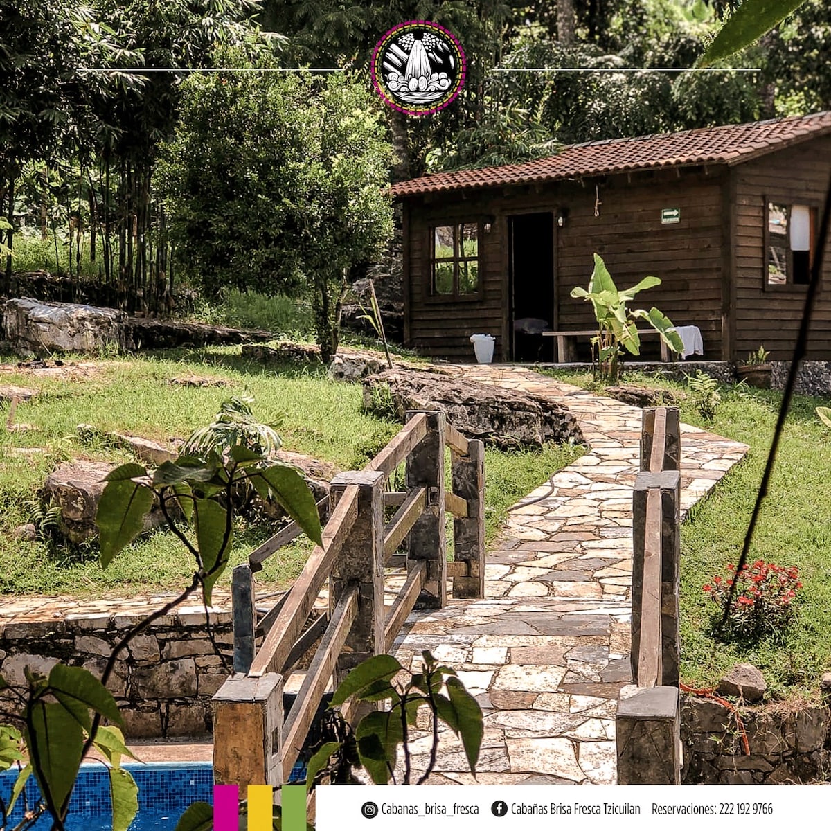 A rustic wooden cabin is set amidst greenery, connected by a stone path lined with vegetation. The area features a tranquil ambiance, with the cabin partially visible behind trees. Natural stone steps lead up to the cabin, enhancing the connection with the surrounding landscape.