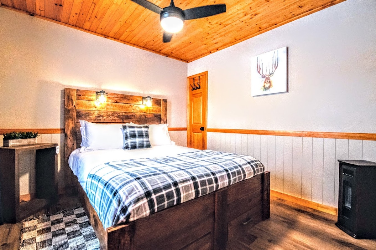 Drift into comfort on a queen-sized bed with a custom barn wood frame, complete with cozy reading lights and an extra blanket for a warm, restful night's sleep.