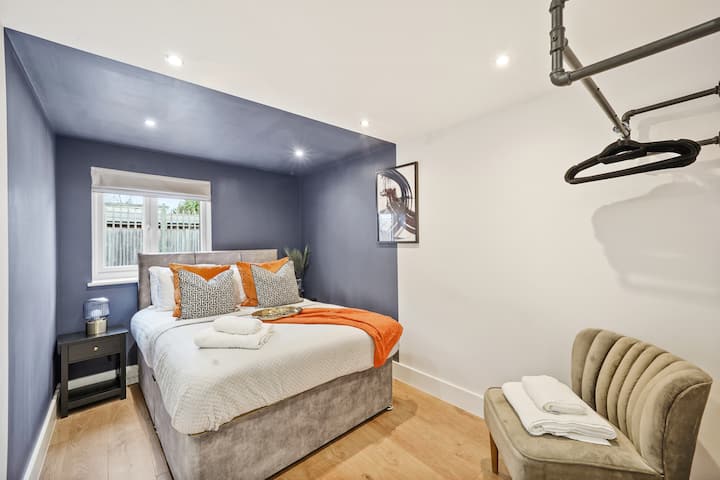 Ukiwa na kuta mahiri za zambarau na mapambo ya kisasa, chumba hicho kinakamilishwa na vivutio vya rangi ya chungwa. Kiti cha kustarehesha kinatoa sehemu nzuri ya kusoma au kupumzika, wakati kabati la nguo lililo wazi linatoa hifadhi rahisi kwa ajili ya vitu vyako.