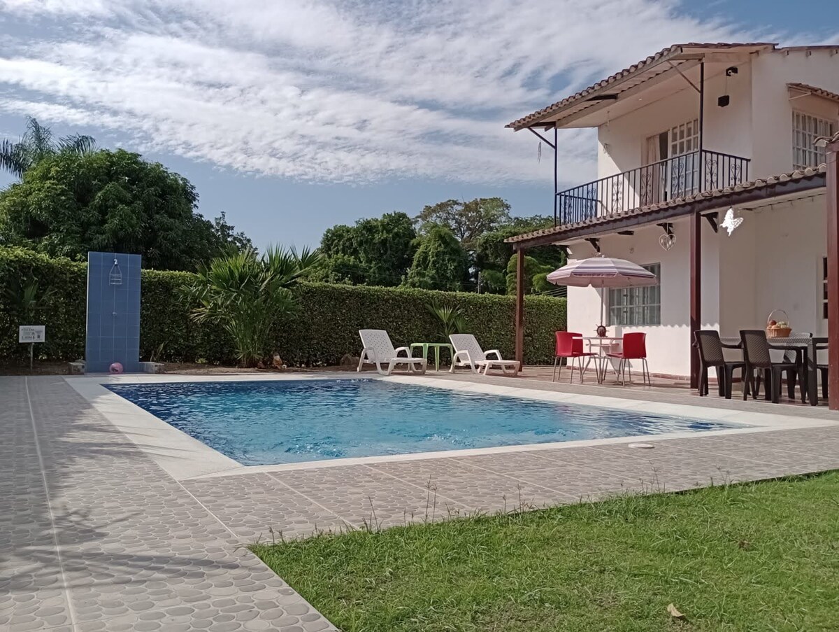 A spacious outdoor area features a private swimming pool surrounded by lounge chairs and a dining set. The two-story house provides access to a covered patio, and well-maintained landscaping enhances the serene atmosphere.