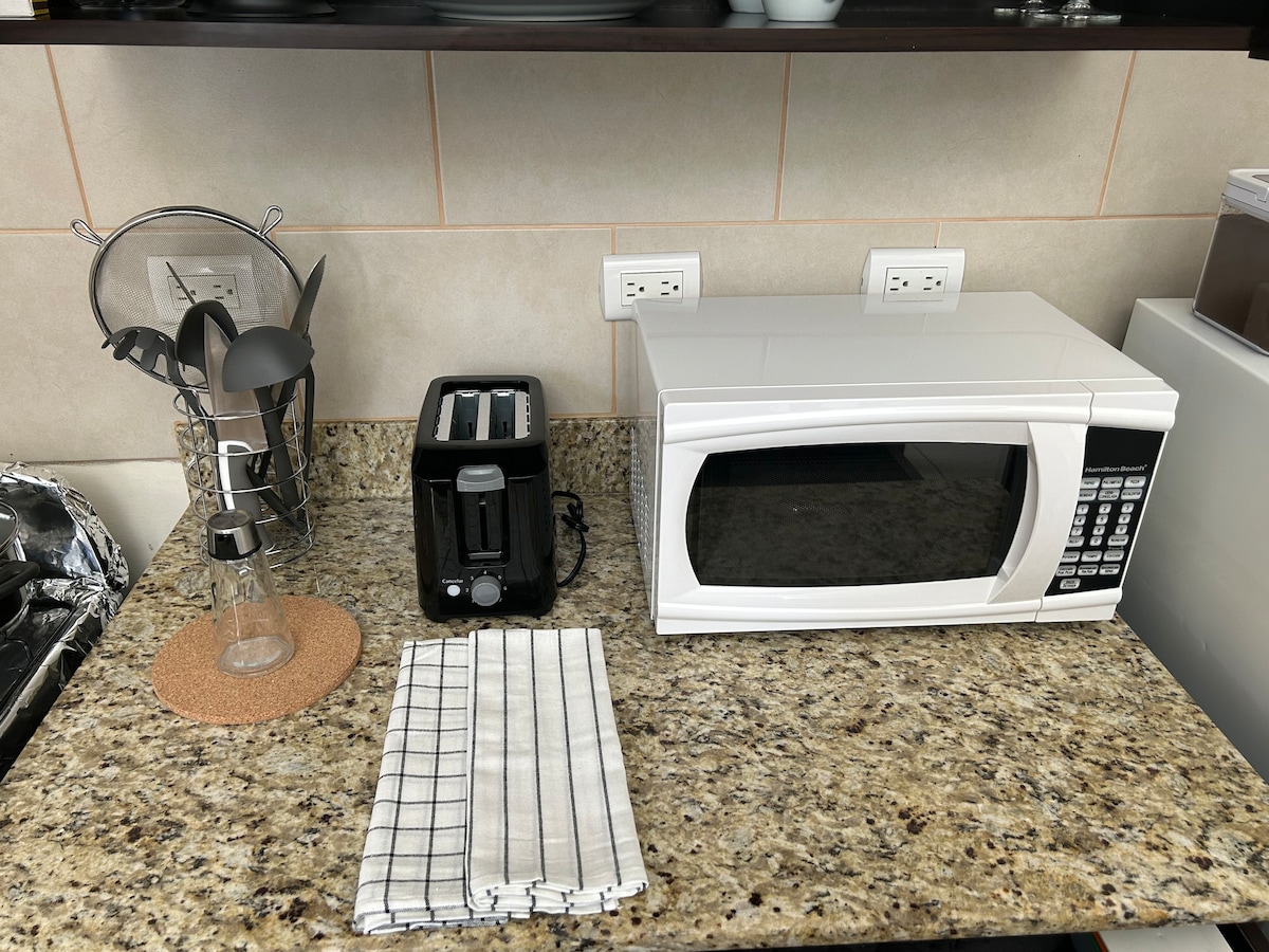 The kitchen countertop showcases essential appliances, including a microwave and a toaster. A coffee maker is accompanied by a glass bottle and a cork coaster. A striped dish towel lies folded beside them, placed on the granite surface.