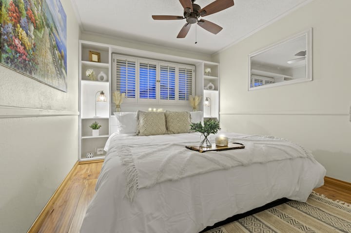 Rilassati in un letto matrimoniale grande con biancheria da letto immacolata, completato da elementi di arredo accuratamente posizionati. La luce soffusa del comodino esalta l'atmosfera tranquilla, mentre le pareti bianche e il caldo pavimento in legno creano uno spazio sereno e invitante.