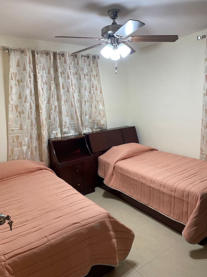 Rum med två enkelsängar, garderob, luftkonditionering och fläkt i taket.