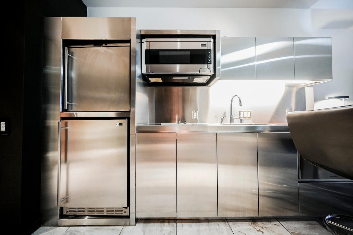 A sleek kitchenette features stainless steel appliances, including a full-height refrigerator, microwave, and a compact sink. The cabinetry provides ample storage space, and the countertop offers a clean and functional workspace for meal preparation.