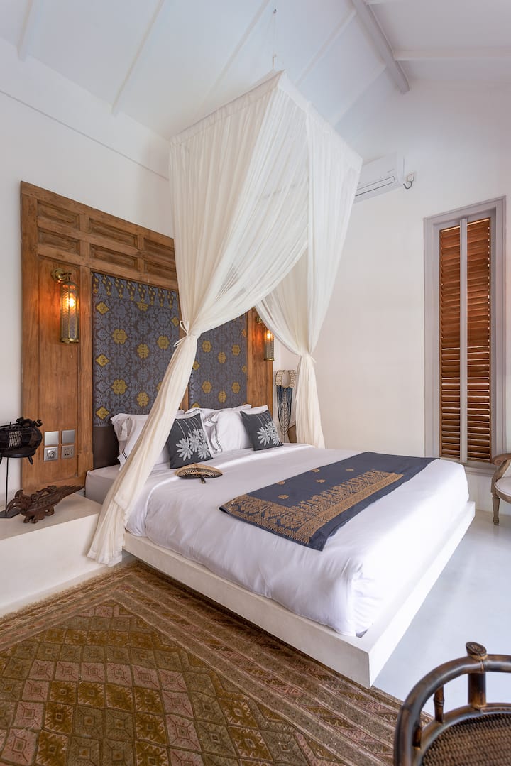 ห้องนอนที่ 4 พร้อมวิวสระว่ายน้ำและประตูกระจก มีเตียงคิงไซส์พร้อมหลังคา หัวเตียงทำมือ และที่นอน ผ้าปูที่นอน และหมอนคุณภาพสูง แสงไฟอบอุ่น สัมผัสวินเทจ และบรรยากาศเงียบสงบเหมาะสำหรับการพักผ่อน