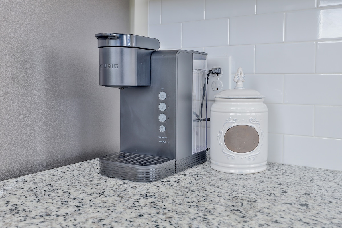 A modern coffee maker is positioned on a granite countertop, accompanied by a decorative white canister. The backsplash features white subway tiles, contributing to a clean and functional kitchen space.