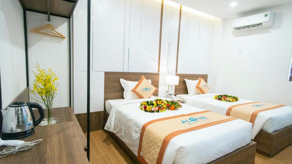 The room features two single beds adorned with floral arrangements. A compact workspace is visible to the side, displaying a kettle and decorative flowers. The air conditioning unit and light fixtures contribute to a well-lit environment, enhancing the overall spaciousness of the area.
