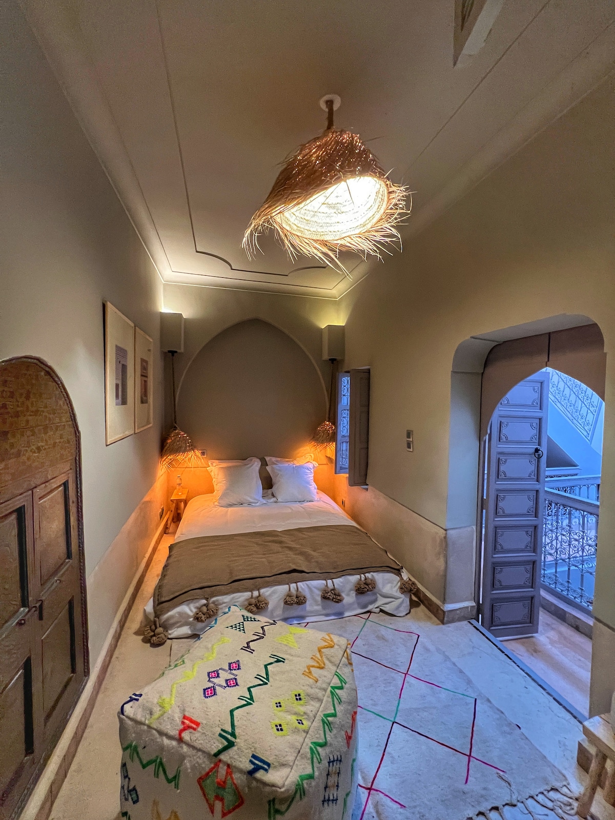 Chambre élégante d'un riad de Marrakech, lit queen size, mobilier en bois sculpté et touches de doré, ambiance sereine.