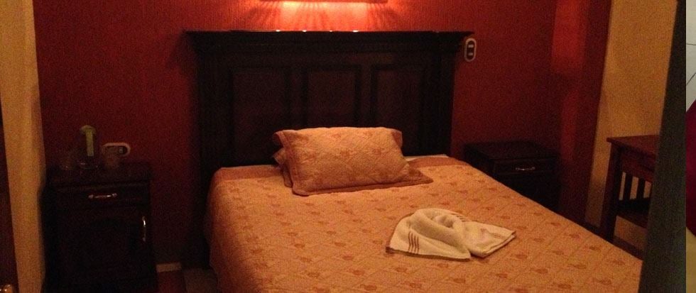 A compact sleeping area is highlighted by warm orange walls. A dark wooden headboard supports a neatly made bed featuring decorative bedding. Nightstands flank the bed, each with small lamps. A towel is placed artfully on the bed, contributing to a tidy appearance.