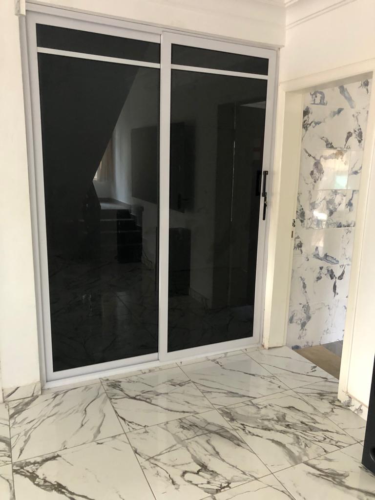 A spacious entrance area features sleek black sliding doors, accentuating a modern design. The floor is covered in glossy marble tiles marked by subtle white and grey veining, while a matching wall adds a touch of elegance.