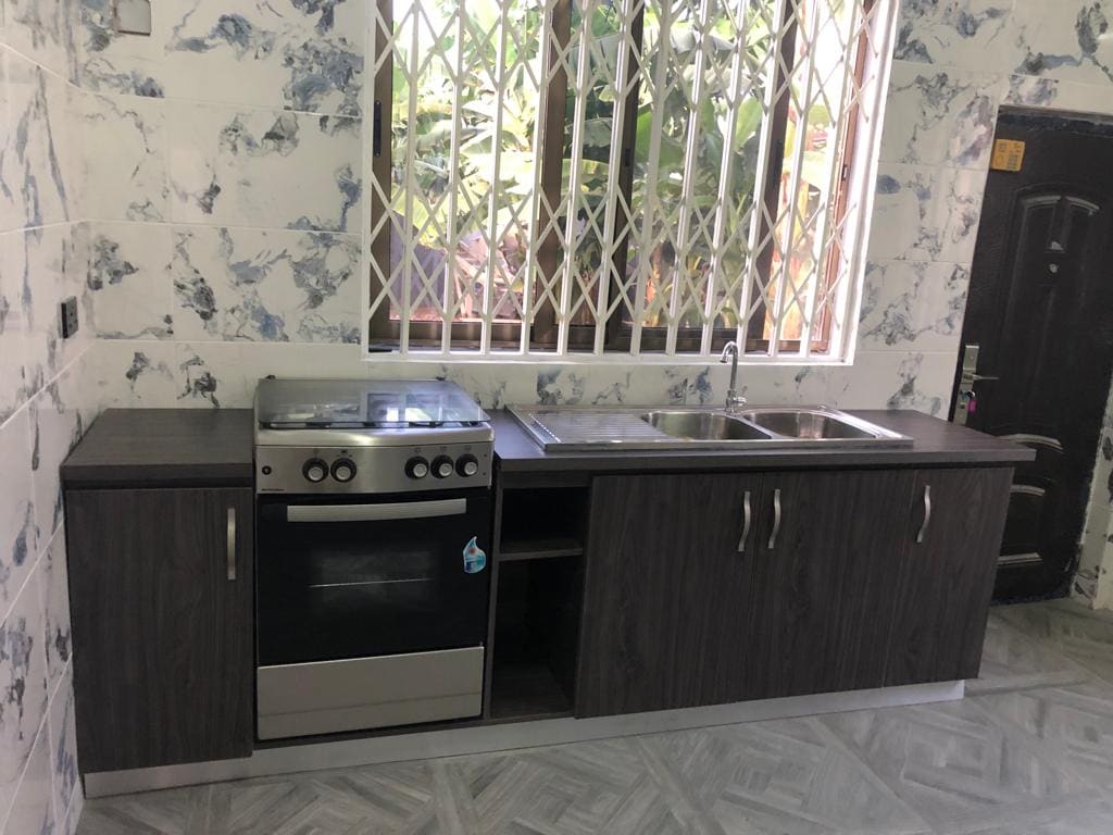 A functional kitchen space is presented with dark wooden cabinetry and a stovetop range. A stainless steel oven is positioned beside a double sink, providing practical amenities. A window allows natural light to illuminate the room, while security bars enhance safety.