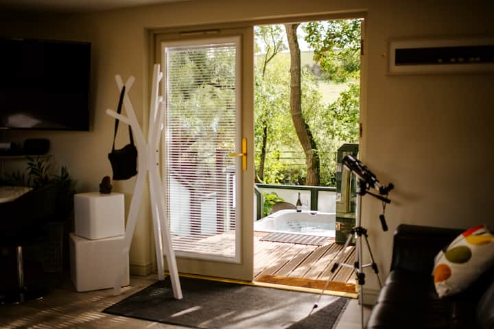 Francúzske dvere zo salónika/spálne na terasu s vírivkou v dome Will's Tree House na farme Winchcombe Farm. Vírivka je na ľahko prístupnej súkromnej vyvýšenej terase vysoko nad lesom a s celoročným výhľadom na koruny stromov. 