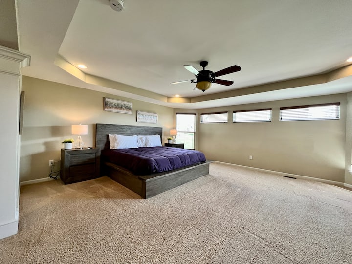 Una vista de tu enorme dormitorio principal espacioso, con abundante luz natural, ventilador de techo, mesitas de noche y cómoda para mucho espacio de almacenamiento. 