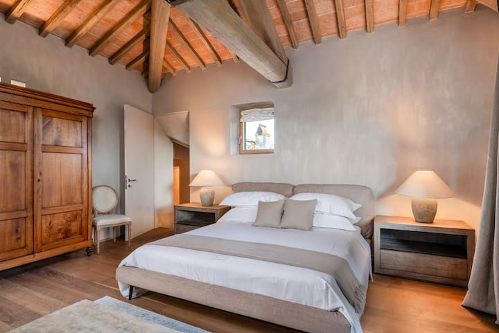La suite La Torretta cuenta con vigas de madera expuestas, suelos de madera cálida e iluminación suave, creando un refugio acogedor y elegante con un carácter toscano atemporal.