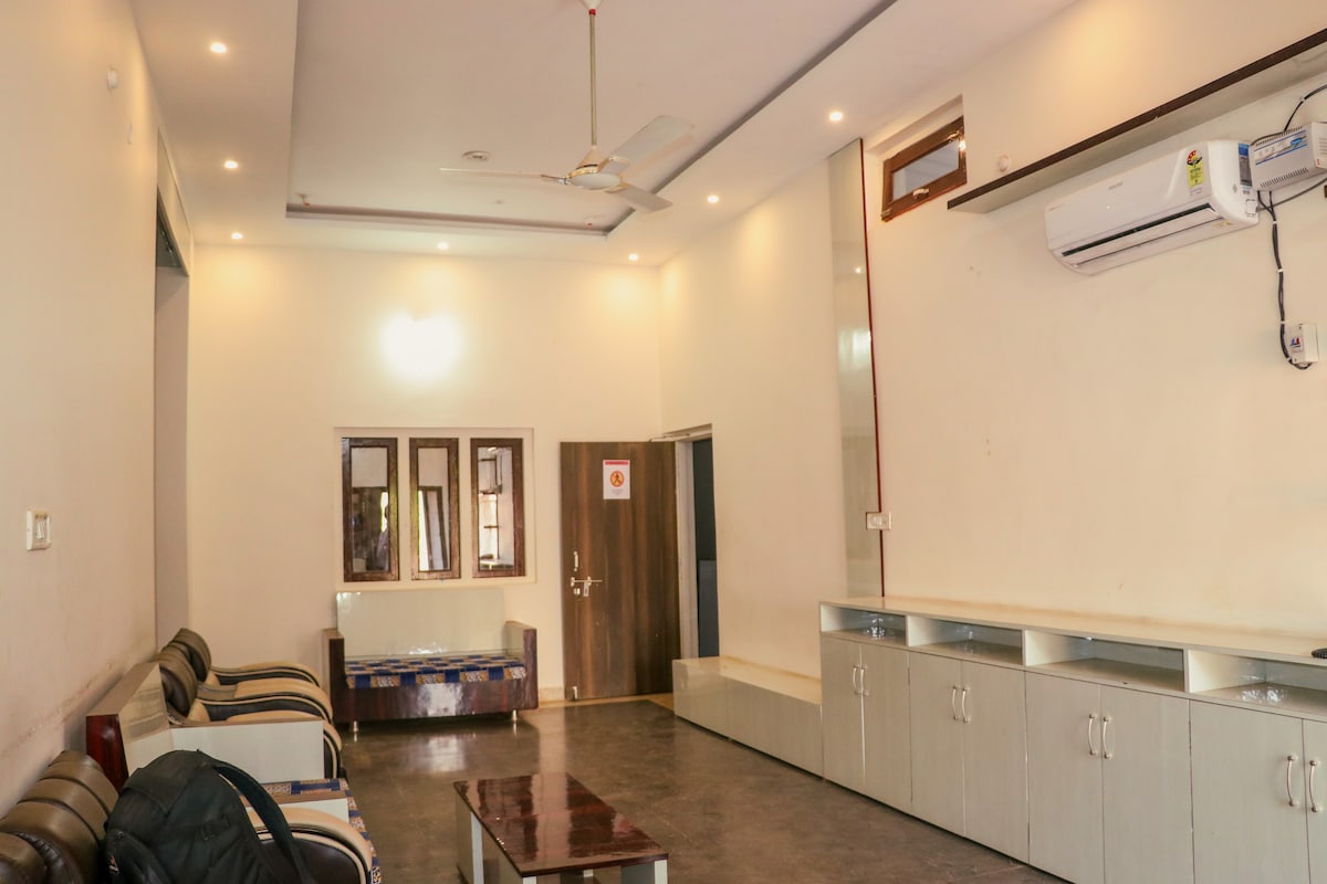 A spacious living area is featured, showcased with contemporary furnishings. Two comfortable sofas are arranged around a wooden coffee table. Light-colored walls and a ceiling fan enhance the bright ambiance, while cabinets line a side wall, offering additional storage.