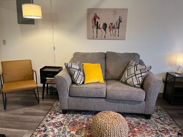 A cozy seating area features a gray sofa adorned with patterned throw pillows, complemented by a decorative pouf. An accent chair in a warm tone and a small side table complete the space, which is illuminated by soft lighting and highlighted by colorful area rugs.