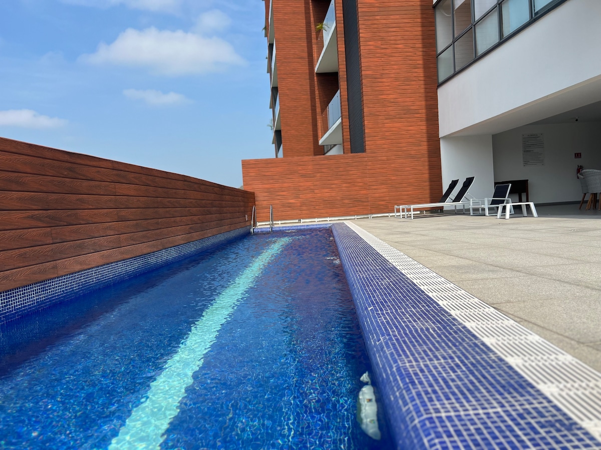 A sleek swimming pool is showcased, featuring vibrant blue tiles and a lengthwise lane for swimming. A smooth stone deck surrounds the pool, with lounge chairs positioned nearby. A wooden wall provides a contrast, enhancing the modern aesthetic of the outdoor space.