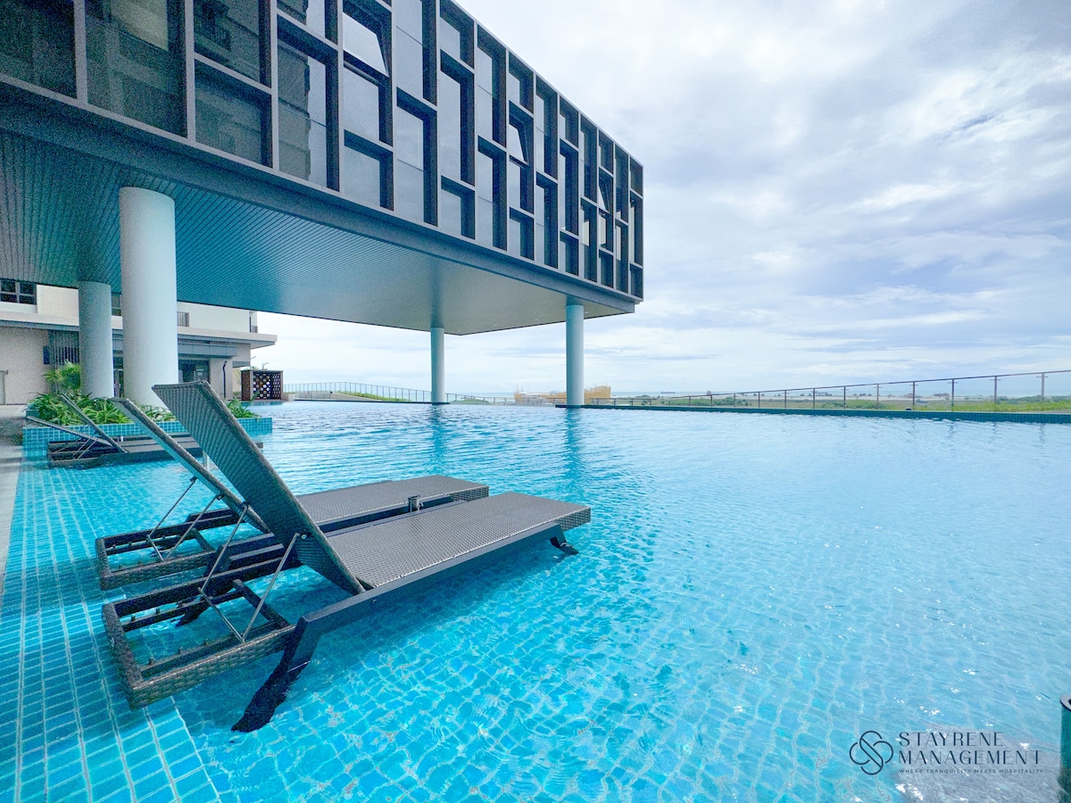 An outdoor swimming pool is visible, featuring clear blue water and lounge chairs positioned at the edge. The pool area is surrounded by lush greenery and a modern building structure looms overhead, creating a visually appealing contrast.