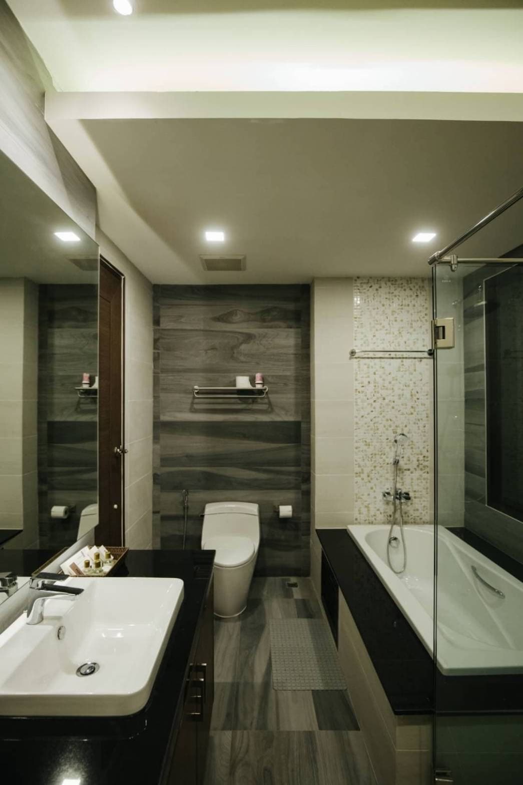 A modern bathroom featuring a glass-enclosed shower and a white bathtub. The dark cabinetry contrasts with light-colored walls. A mirrored wall enhances the sense of space, while neatly arranged toiletries on the countertop add functionality.