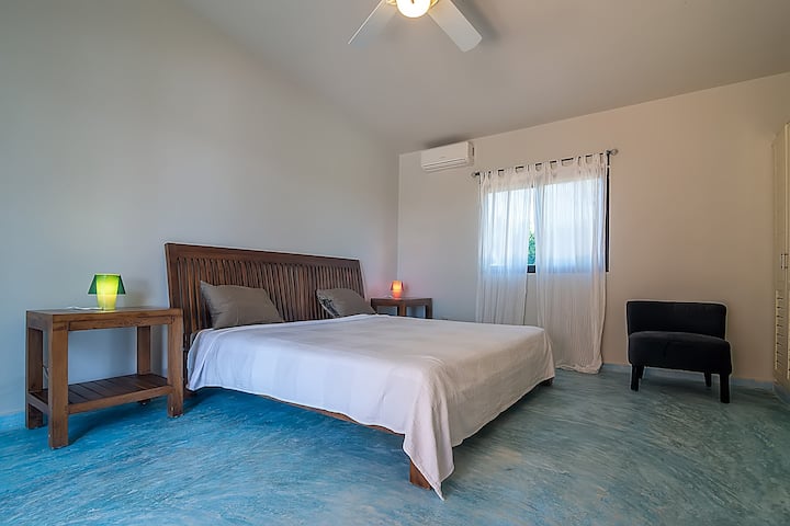 Пространа спална соба со брачен кревет, клима уред и тавански вентилатор, идеална за одмор во мир.