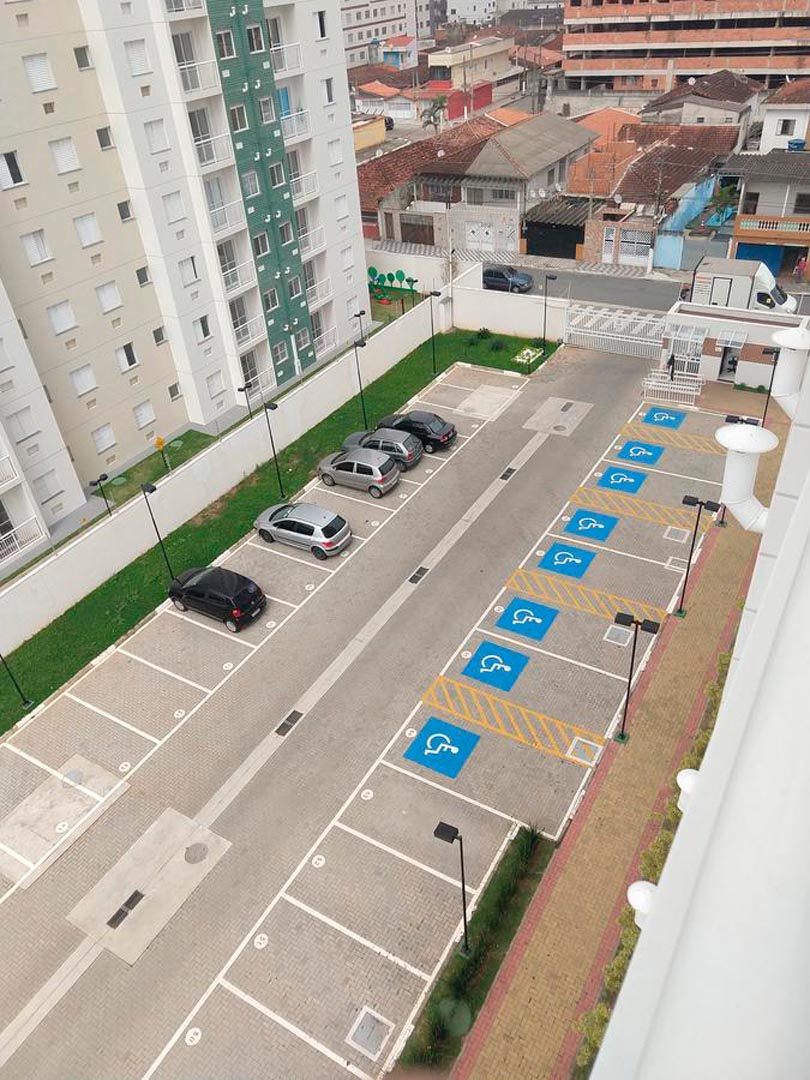 A view from above showcases the parking area of the complex, featuring designated spots including handicapped parking. Several vehicles are parked in marked spaces, with well-maintained paver stones visible throughout the area. Surrounding greenery adds a touch of nature to the setting.