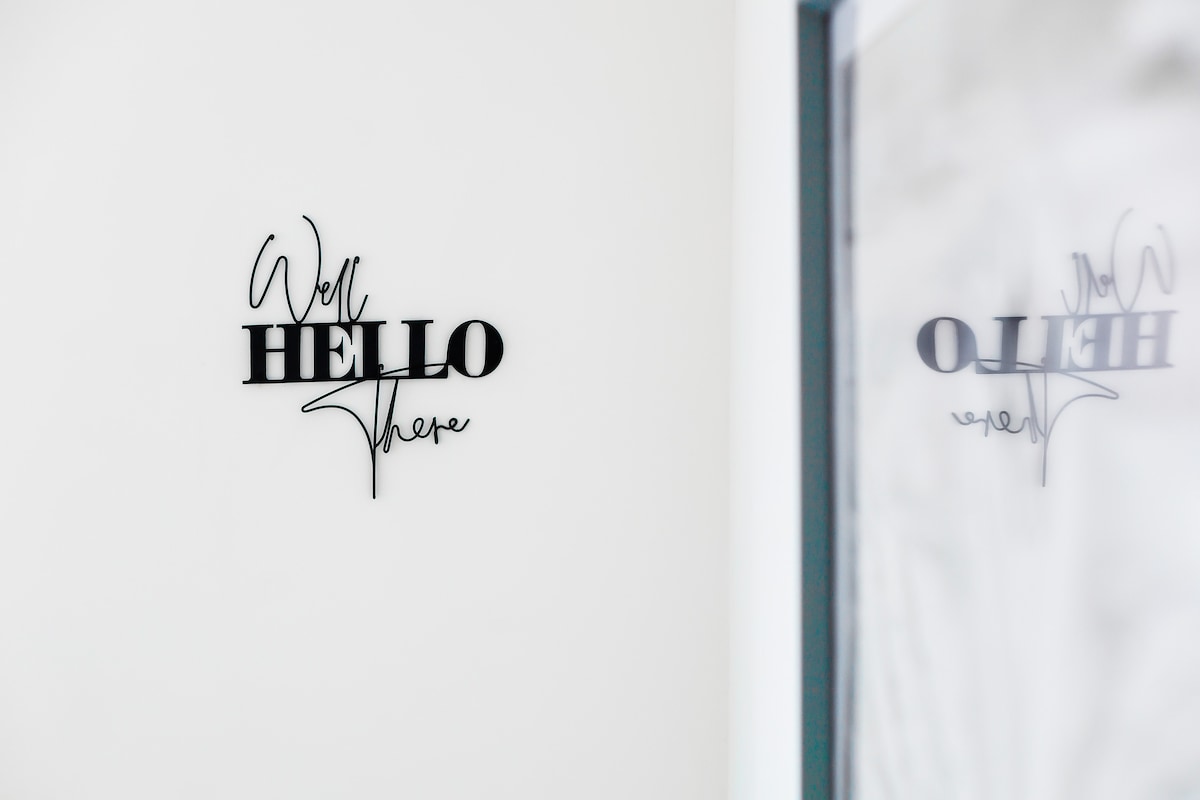 A stylish wall display features a modern black sign with the text 'Well Hello There,' creating a welcoming focal point in the entrance area. The clean, neutral background further enhances the contemporary aesthetic of the space.