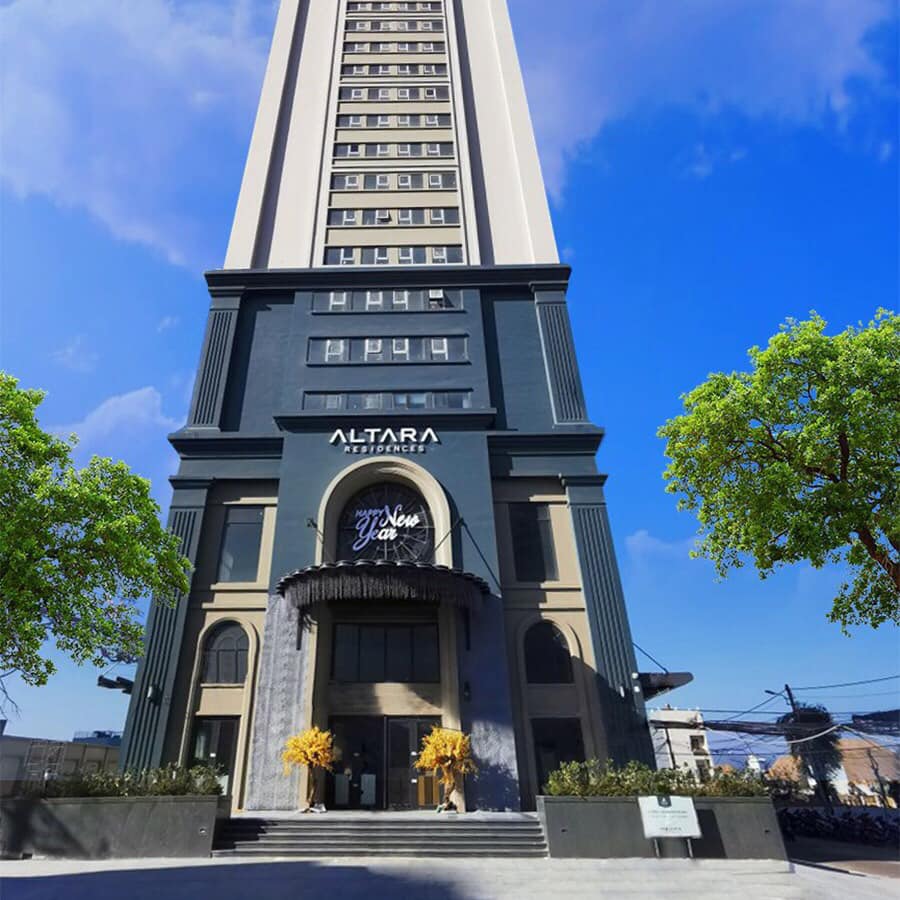 A modern high-rise building features a prominent entrance framed by well-maintained greenery. The facade displays a sleek design, with large windows allowing natural light. Clear blue skies provide a bright backdrop, highlighting the building's stature in the urban landscape.
