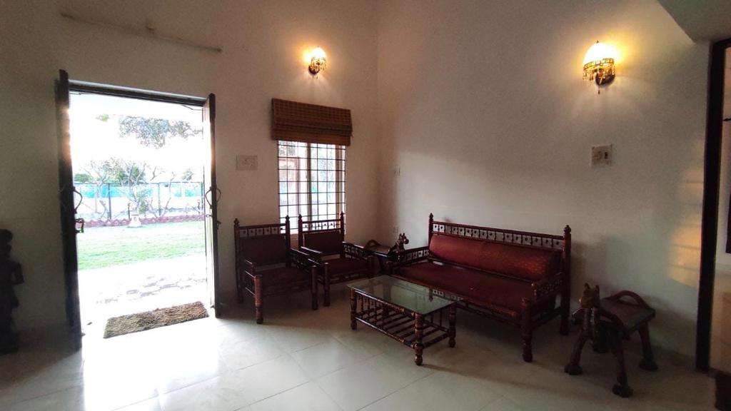 A welcoming sitting area is presented with traditional wooden furniture, including a sofa and chairs. A glass coffee table is positioned in the center, reflecting natural light from the doorway. The decor is complemented by wall sconces providing soft illumination.