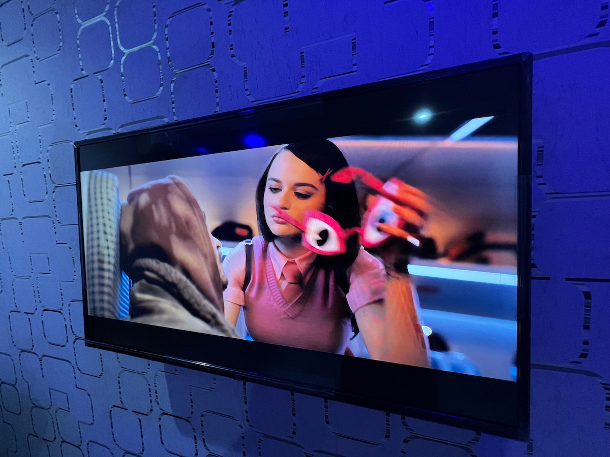 A flat-screen television is mounted on a textured wall exhibiting a modern design. The screen displays a colorful scene from a film, illuminated by blue ambient lighting that enhances the viewing experience.