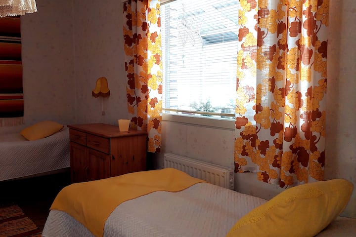 Dormitorio amarillo. Dos camas individuales y
ventana con una persiana y una cortina opaca.