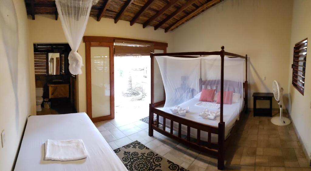The room features one king bed and one single bed, both draped with white mosquito nets. A ceiling fan circulates air, and large sliding doors provide access to a terrace. The floor is tiled, and a small table is positioned next to the single bed.