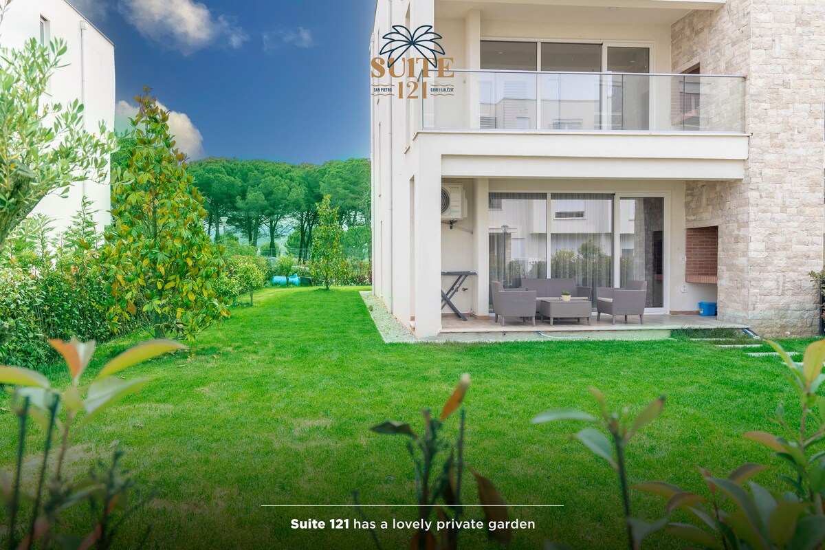 A private garden is presented, featuring well-maintained grass and a variety of greenery, including small trees and shrubs. The garden offers a seating area with outdoor furniture, inviting a peaceful space for relaxation. The backdrop showcases distant trees, contributing to a serene environment.
