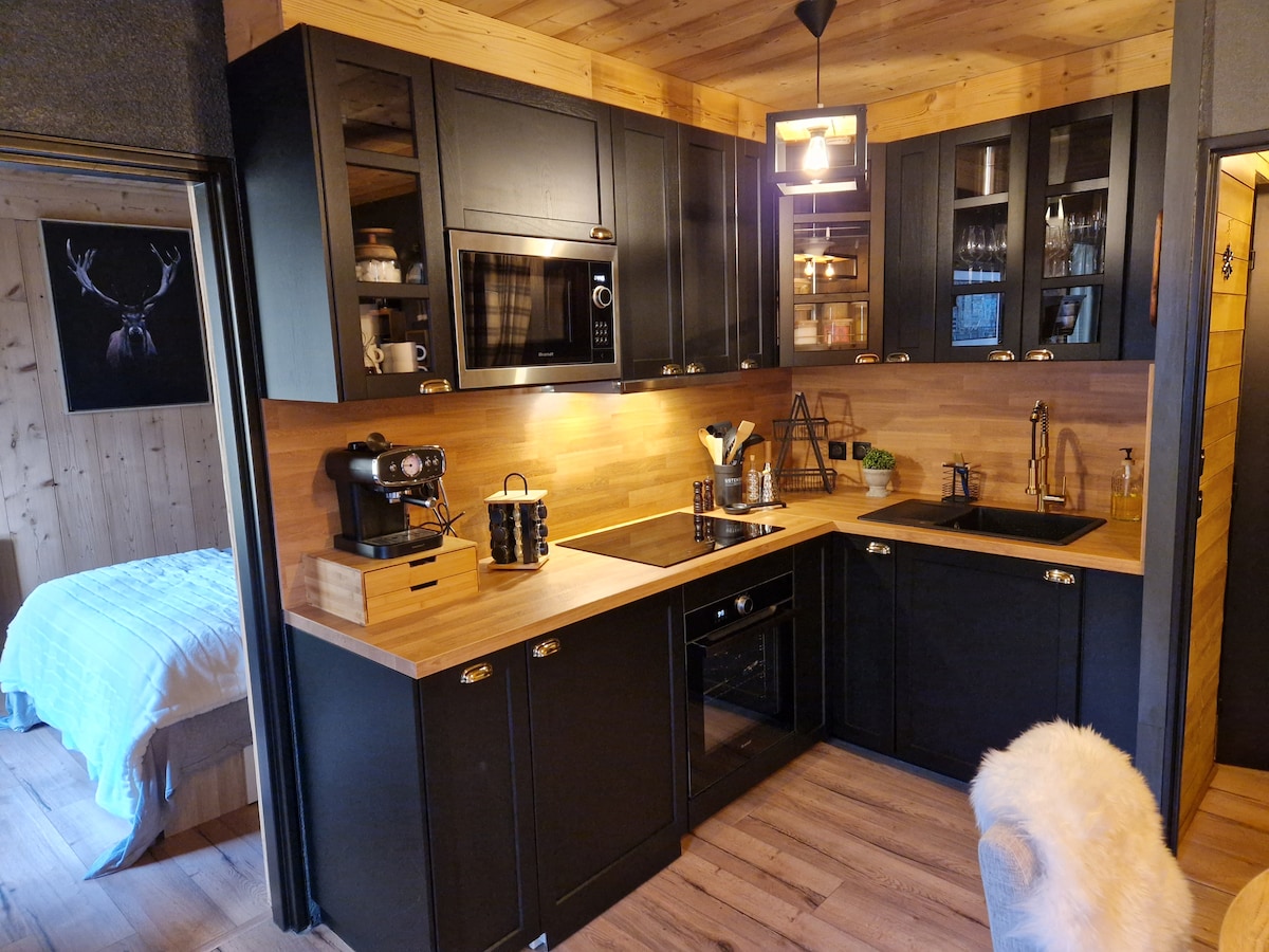 A modern kitchen features sleek black cabinetry and warm wooden accents. Equipped with essential appliances, including a microwave and stovetop, the space showcases a stylish coffee maker and tasteful decor. Soft lighting adds to the inviting ambiance, enhancing the kitchen's functionality and charm.