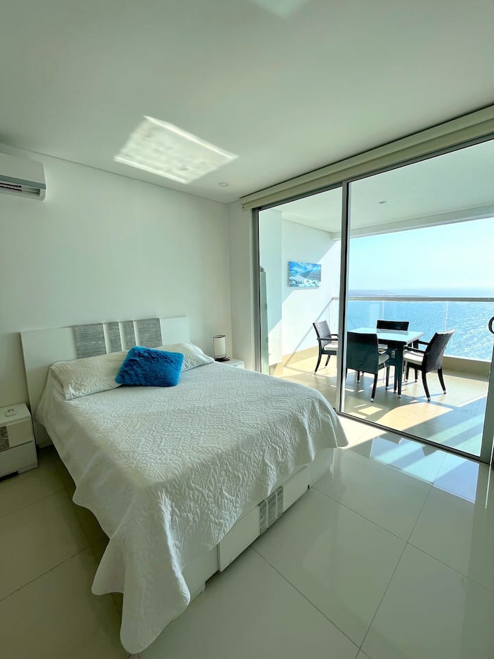 Retirez-vous dans le confort de la chambre principale, avec un grand lit et un accès direct au balcon pour une vue matinale.