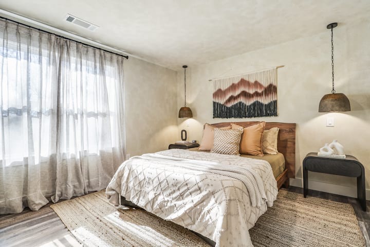 Relax in a comfortable queen bed, surrounded by hanging lights, and natural light from sheer curtains.