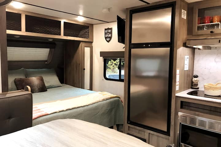 Nga e majta në të djathtë: tavolinë ngrënieje, dhomë gjumi me një krevat dopio "RV queen", frigorifer dhe frigorifer,  kuzhinë me mikrovalë. 