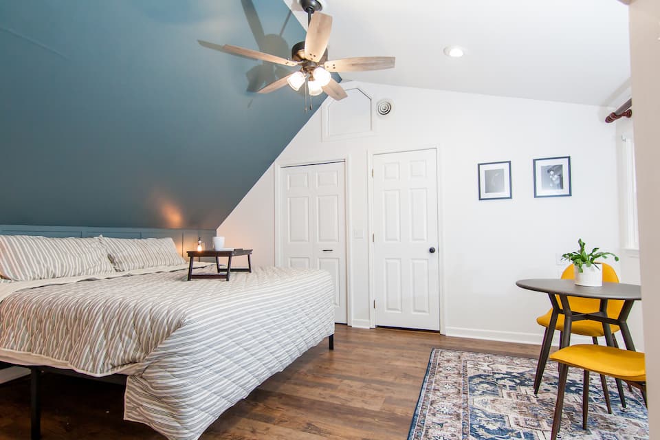 King bed under the vaulted ceiling with a small table by the window