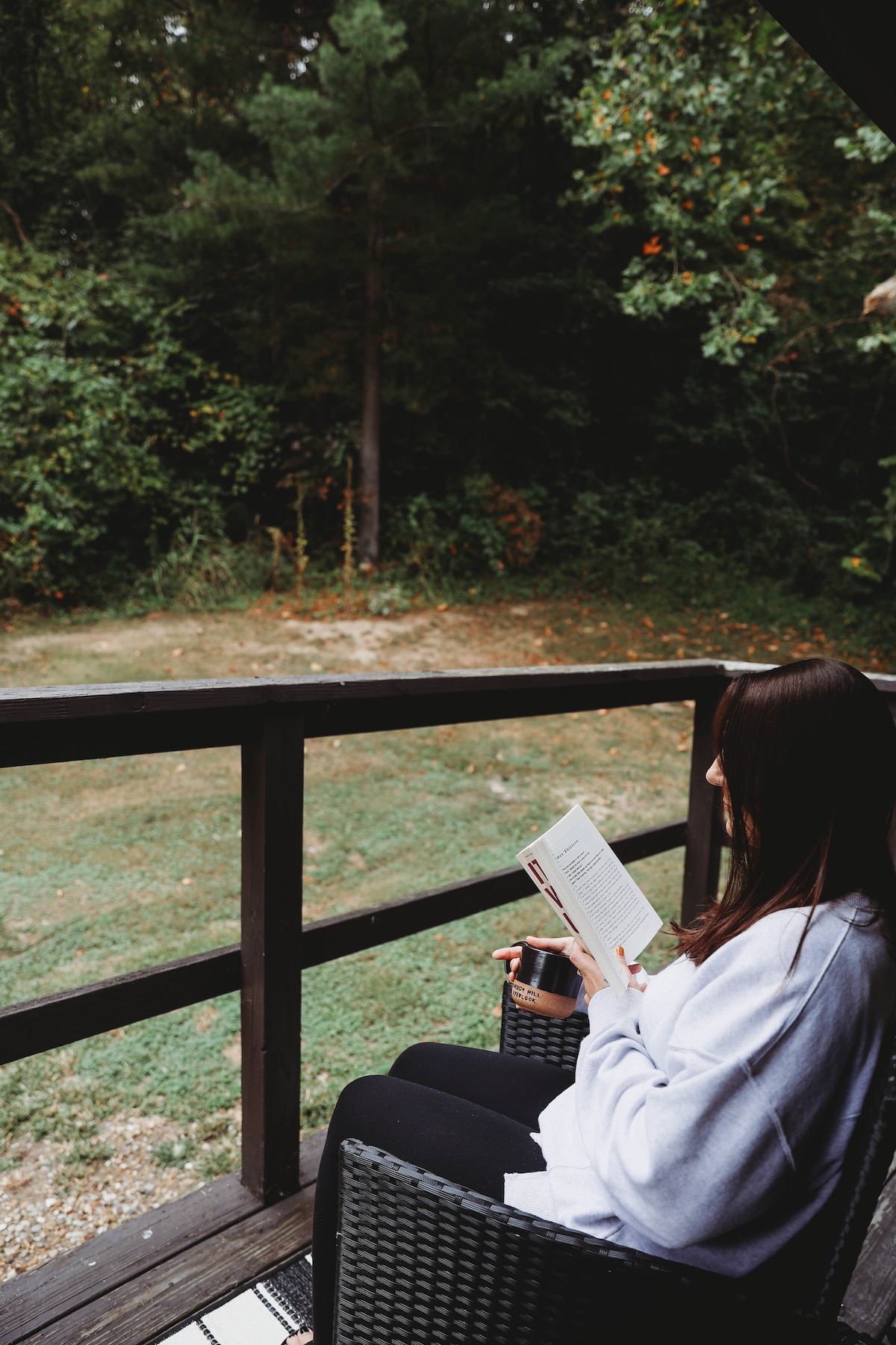 A person sits comfortably on a wicker chair on the porch, reading a book. The view features a serene outdoor space with greenery and a gravel path, creating a tranquil atmosphere for relaxation.