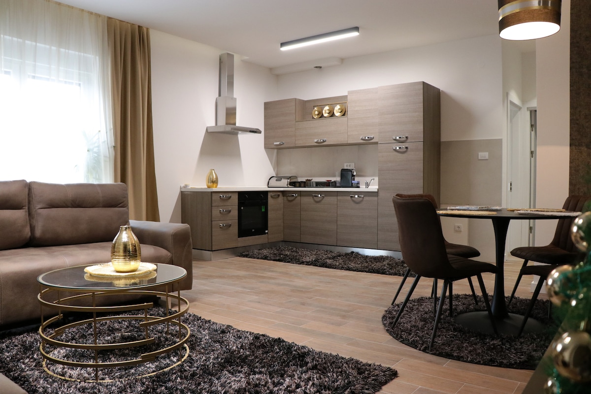 A modern living area is depicted with a comfortable sofa and a round dining table, surrounded by stylish chairs. The kitchen features sleek cabinetry and essential appliances. Soft textures are introduced by the area rug, while natural light brightens the space through large windows.