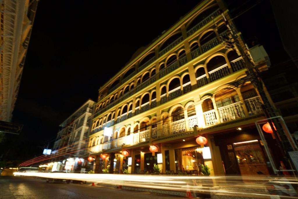 The Grand Orlov hotel is depicted in a well-lit night setting, showcasing its elegant architecture with arched balconies and decorative elements. Soft lighting highlights the structure, while nearby street features and lantern decorations add a vibrant touch to the atmosphere.