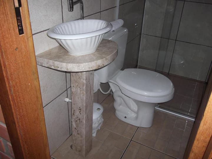 PETITE SALLE DE BAIN AVEC BOÎTE EN VERRE. AU MILIEU DES DEUX CHAMBRES, COULOIR À L'EXTÉRIEUR.