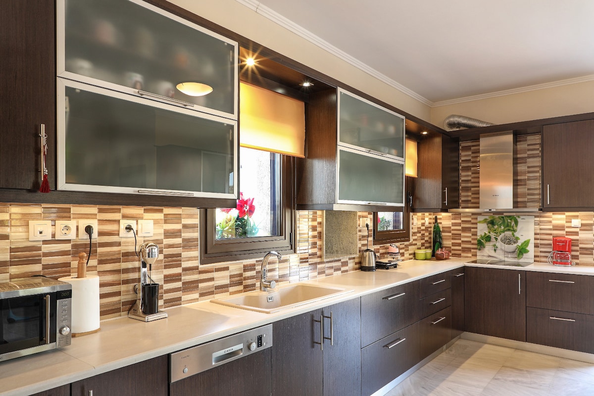 The kitchen is equipped with modern amenities, featuring dark wood cabinetry and sleek countertops. A sturdy sink is positioned in front of a window, with a microwave and other appliances readily available. Under-cabinet lighting illuminates the unique tiled backsplash, enhancing the functional workspace.