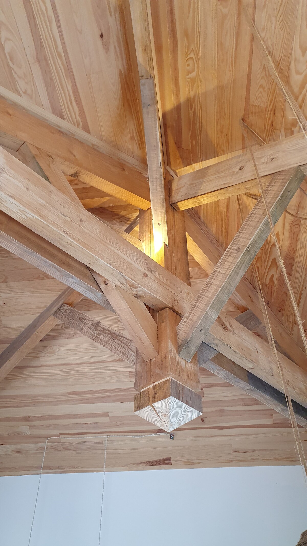 Exposed wooden beams and a central support post are showcased in the ceiling, exhibiting a natural wood finish. Soft lighting is integrated, enhancing the design while illuminating the structural elements above.
