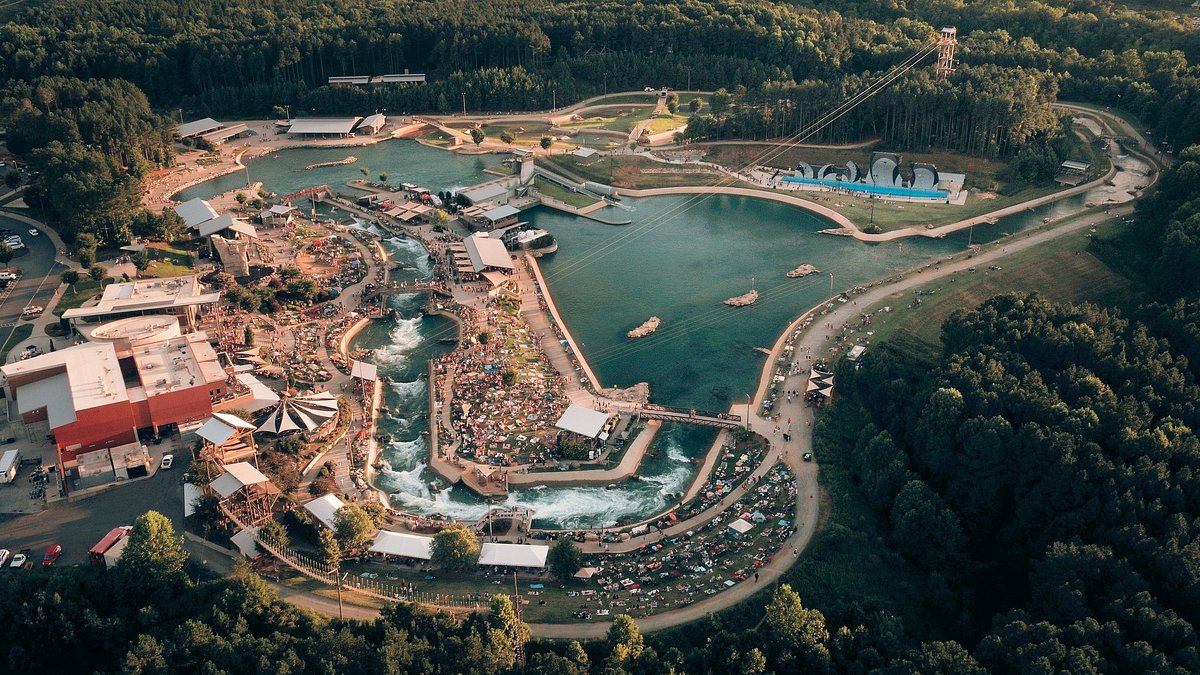 Aerial view of a vibrant water park, featuring multiple large pools and a variety of water attractions. Families and visitors are seen enjoying the park, surrounded by lush greenery. Various structures such as slides and shaded areas can be observed, providing ample entertainment options.