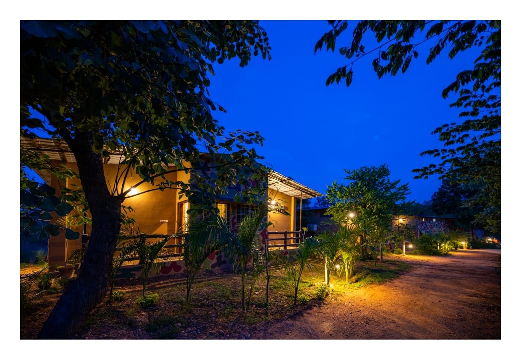 A charming structure is softly illuminated under a night sky, surrounded by lush trees and well-maintained landscaping. Pathway lights guide the way, enhancing the inviting atmosphere of the residence's exterior.