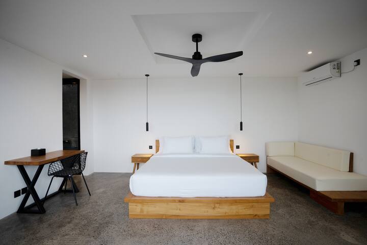 Un dormitorio limpio y minimalista con una cama grande y ventilador de techo, que crea un ambiente tranquilo para descansar.
