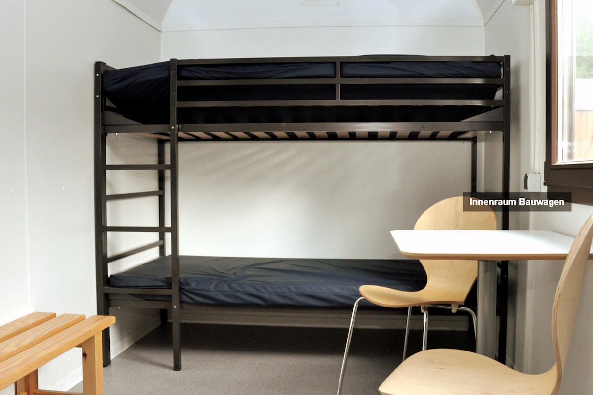 Simple et entouré par la nature, tu dors dans la petite roulotte. 4 couchages, table avec chaises. Minimaliste et pratique.