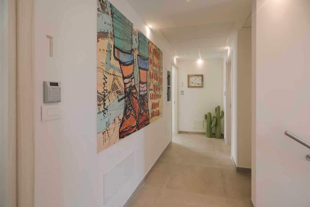 A corridor is highlighted by a large, colorful mural depicting a vibrant design with shoes. Textured flooring leads to various room doors, with simple wall decor including a clock visible. Soft lighting creates a bright and welcoming atmosphere.