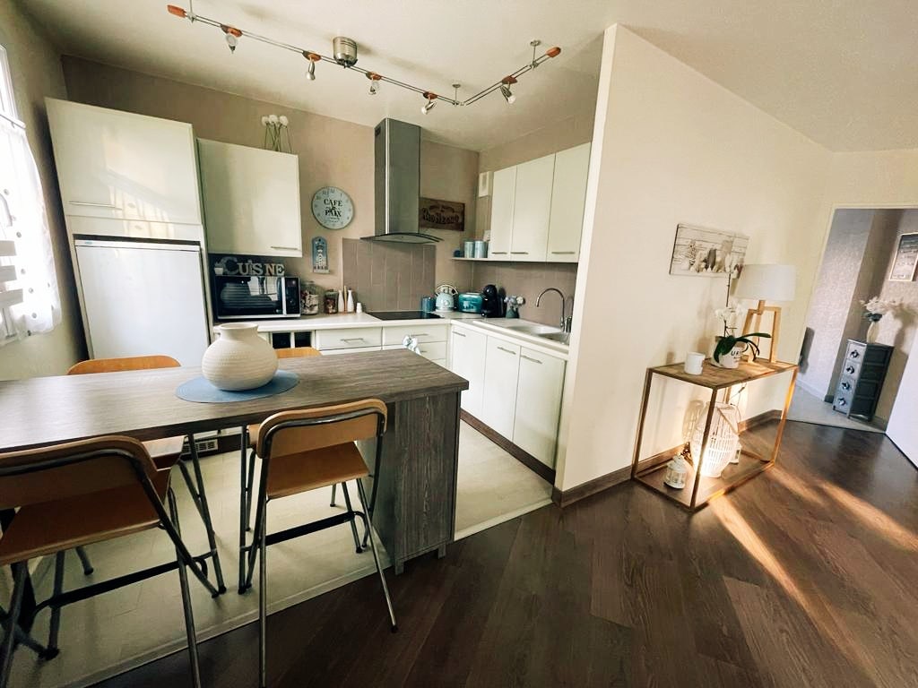 A modern kitchen is highlighted by a central island and two wooden stools. Cabinets and countertops feature a neutral palette, while appliances are neatly arranged. Natural light flows in through a window, creating a bright and inviting cooking space. An additional area with decorative accents is visible.